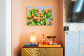 Ein Zimmer mit einer Obstgemäldes an der Wand, einer dekorativen Ablage mit Büchern und einer Kerze, sowie einem an der Wand befestigten Fernseher.