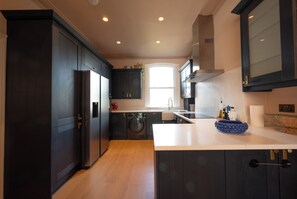 Una cocina moderna con armarios oscuros, un refrigerador de acero inoxidable, una lavadora y un lavamanos.