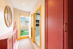 A hallway with a red door, a mirror, and a view of a garden through an open door. - Stylish 2BDR Flat w Private Terrace in White City (Greater London)