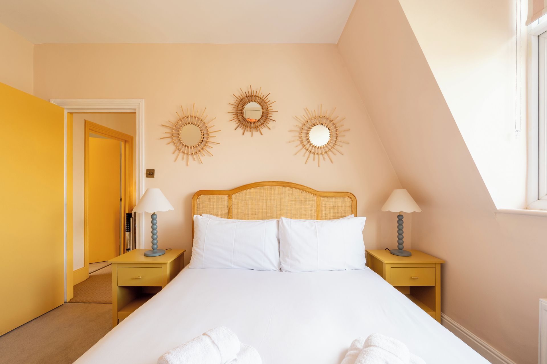 Ein Schlafzimmer mit einem großen Bett, zwei Nachttischen inklusive Lampen sowie drei Wandspiegeln im Sonnenstrahl-Design.