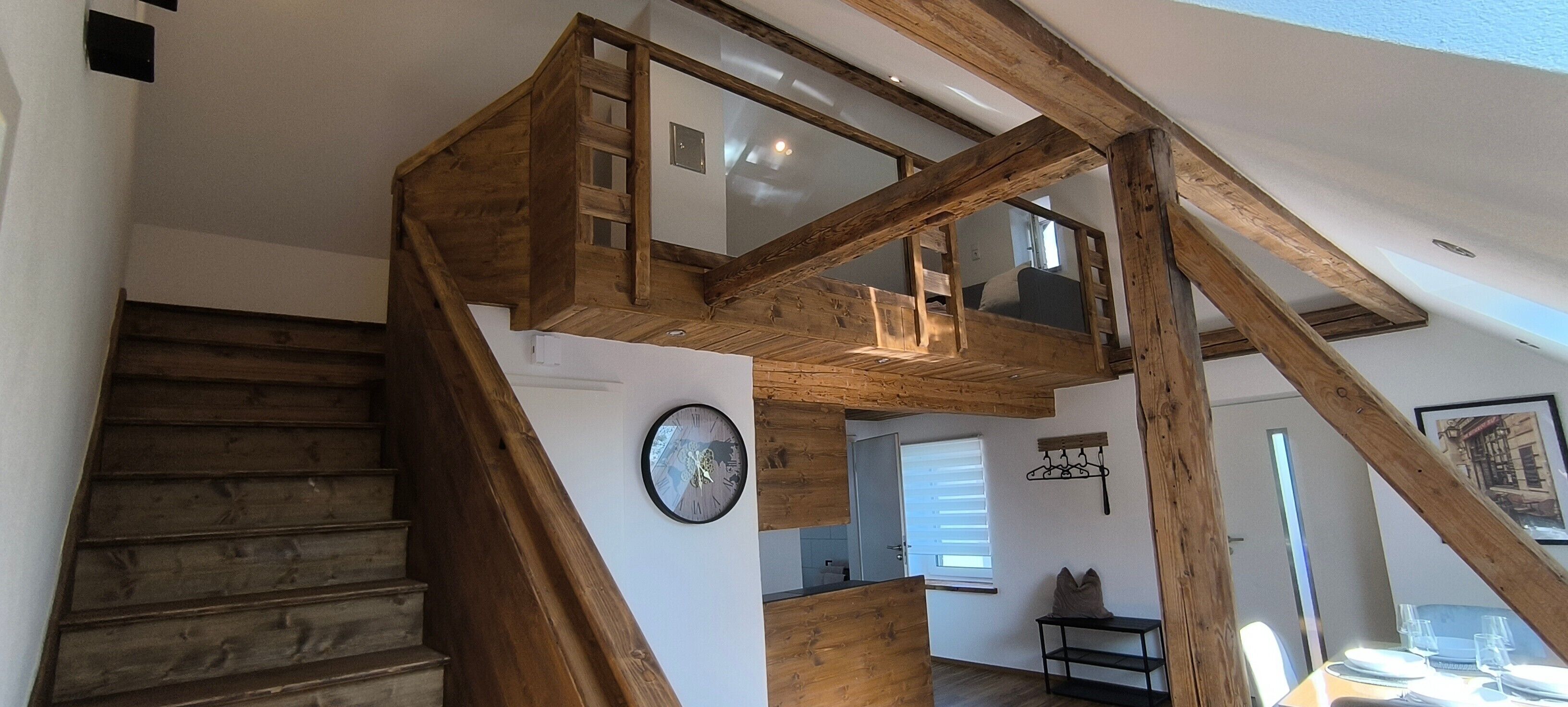 Eine Holztreppe führt zu einem Schlafzimmer auf dem Dachboden, mit einem Bett und einem Fenster.