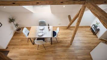 Ein Essbereich mit einem Holztisch, gedeckt für zwei Personen, einem Stuhl, einer Topfpflanze und einem kleinen Tisch mit Büchern und einer Vase.