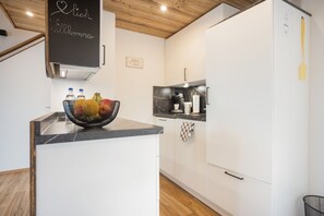 Una cuina moderna amb armaris blancs, una pissarra amb un missatge de benvinguda i un plat de fruita a la barra.