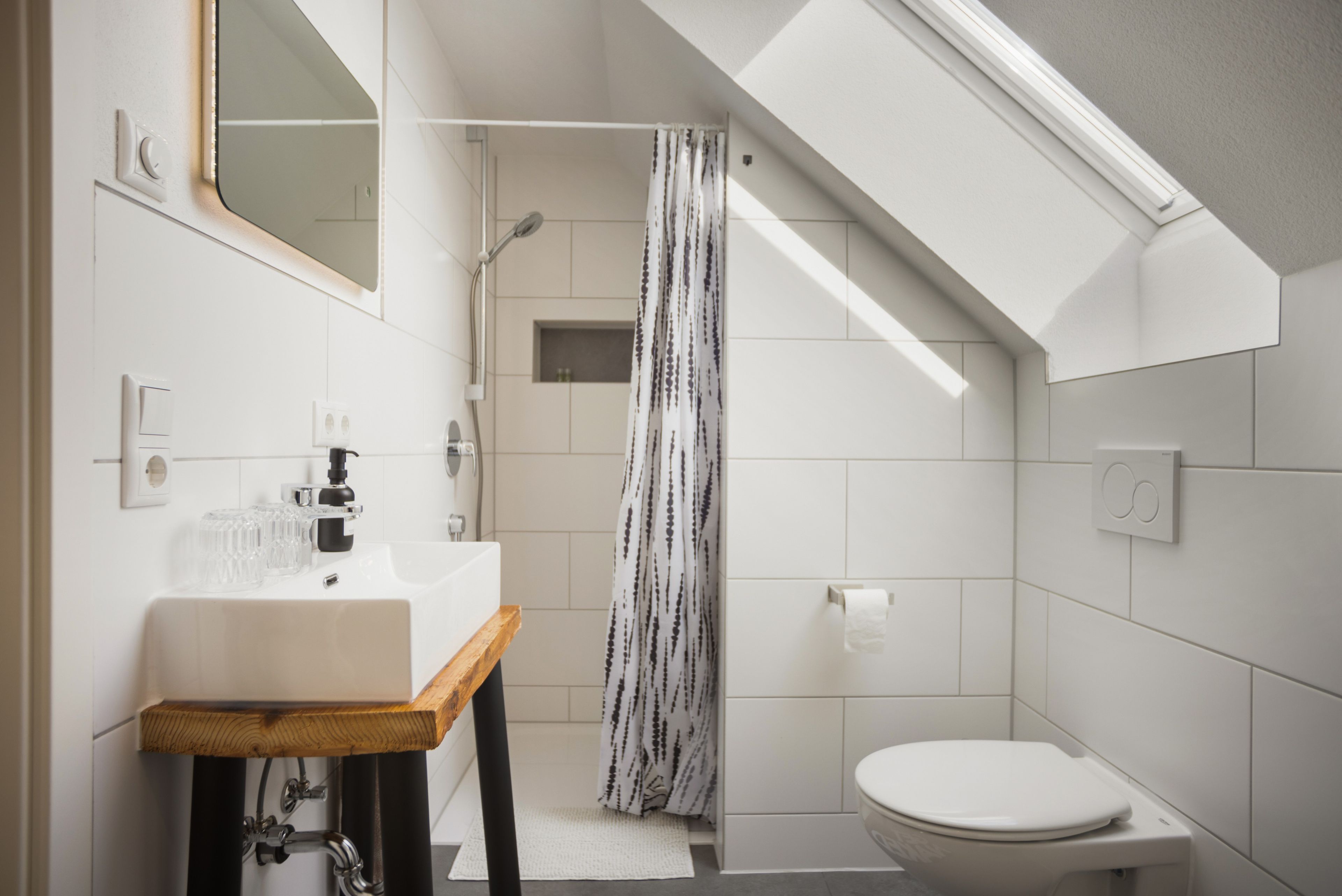 A modern bathroom with a skylight, a shower, a toilet, and a sink with a wooden countertop.