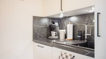 Ett modernt kök med en svart marmorvägg bakom diskbänken, en kaffebryggare, en vattenkokare och en diskho.