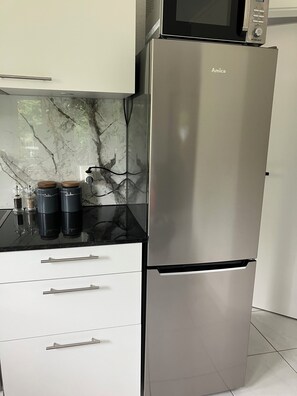 A stainless steel refrigerator with a microwave on top, two black containers with wooden lids, and a marble backsplash. - Apartment with a terrace in the heart of nature (Avenches)