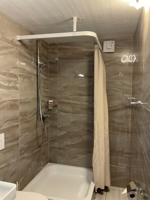 Et badeværelse med bruser, badekar og toilet.