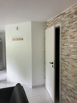 A modern interior with a white wall, a wooden coat rack, a door leading to a room with a brick-patterned wall, and a black sofa. - Apartment with a terrace in the heart of nature (Avenches)