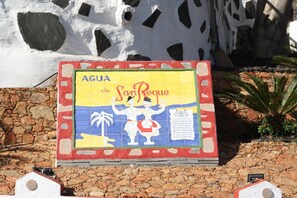 Un letrero colorido con el texto 'AGUA de San Roque' e ilustraciones de personas y palmeras.