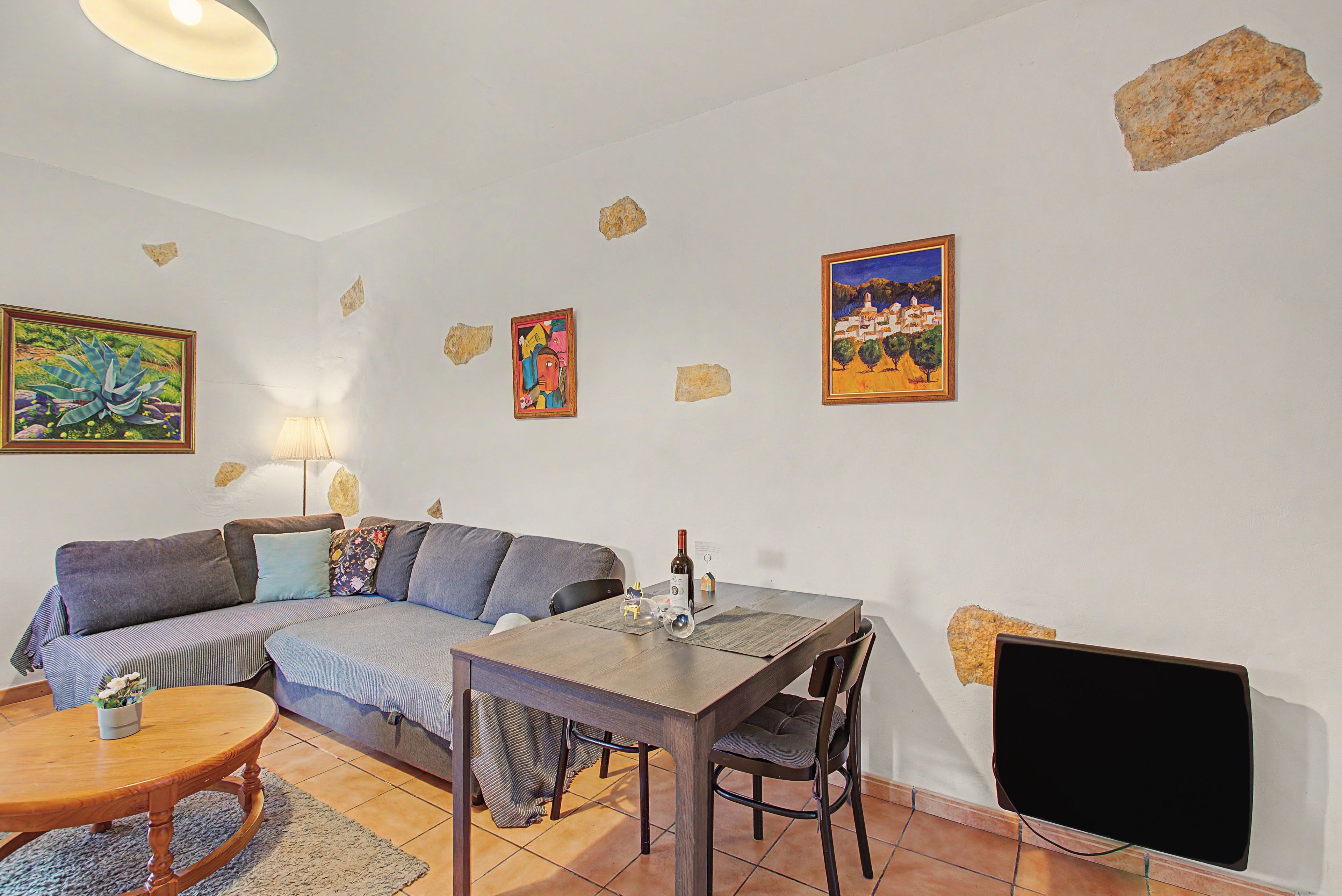 Un salon comprenant un canapé, une table à manger avec des chaises, un téléviseur et des œuvres d’art accrochées aux murs.