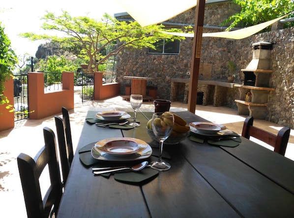 An outdoor dining area with a stone wall, a wooden table set with plates, cutlery, and a glass of water.