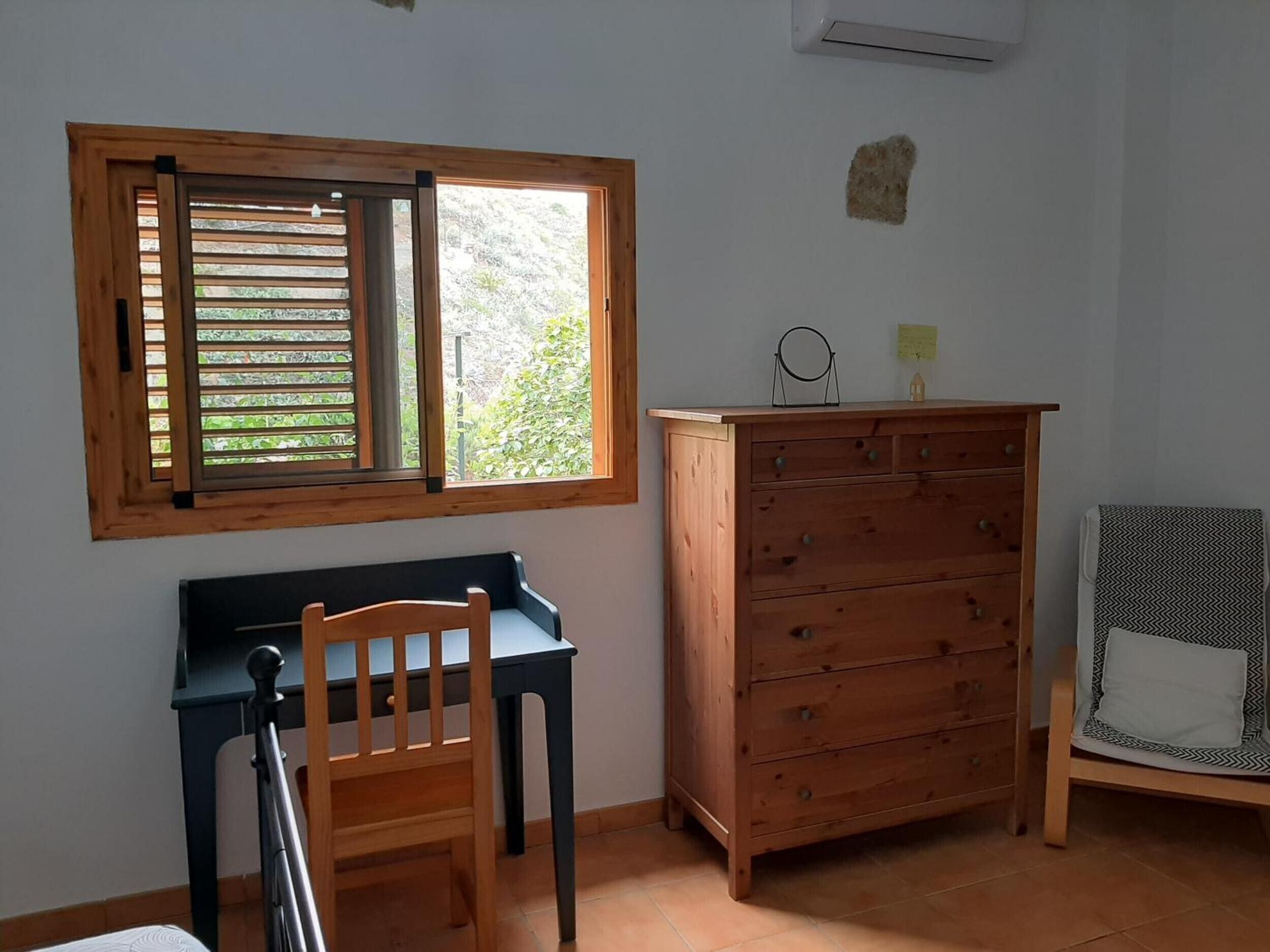 Une pièce avec un bureau en bois, une chaise, une commode et une fenêtre avec des volets en bois.