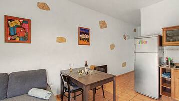 Un espacio habitable compacto con una mesa de comedor, sillas, un sofá, una zona de cocina con refrigerador y dos cuadros colgados en la pared.