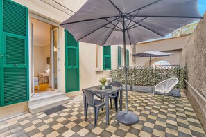 An outdoor patio area with a checkered floor, a table with chairs, and a large umbrella providing shade. - [Timeline Modern] 5Terre by ferry (La Spezia)
