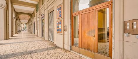 A corridor with a tiled floor, a wooden door with glass panels, and a wall-mounted information board.