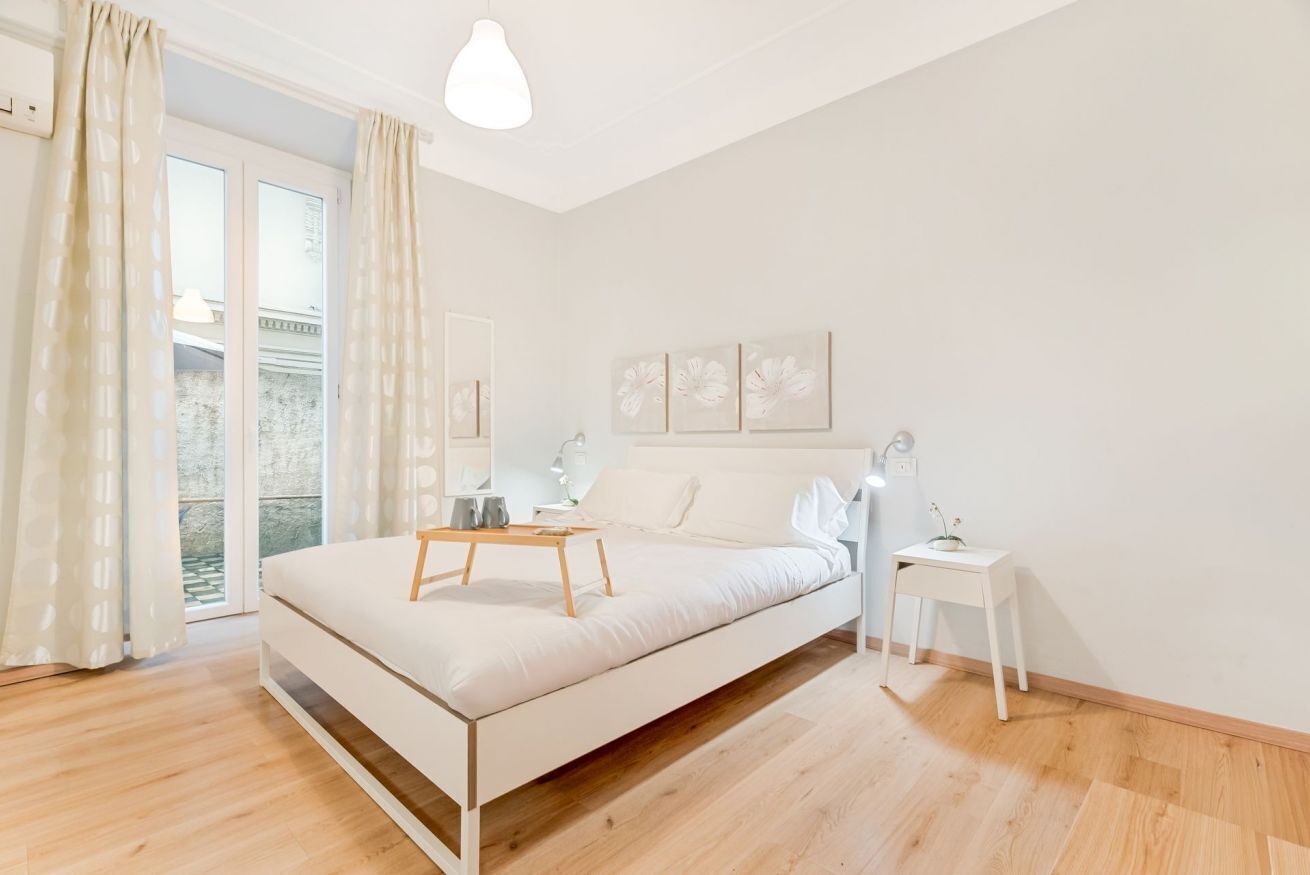Een minimalistisch ingerichte slaapkamer met een bed, nachtkastjes en uitzicht door een raam.