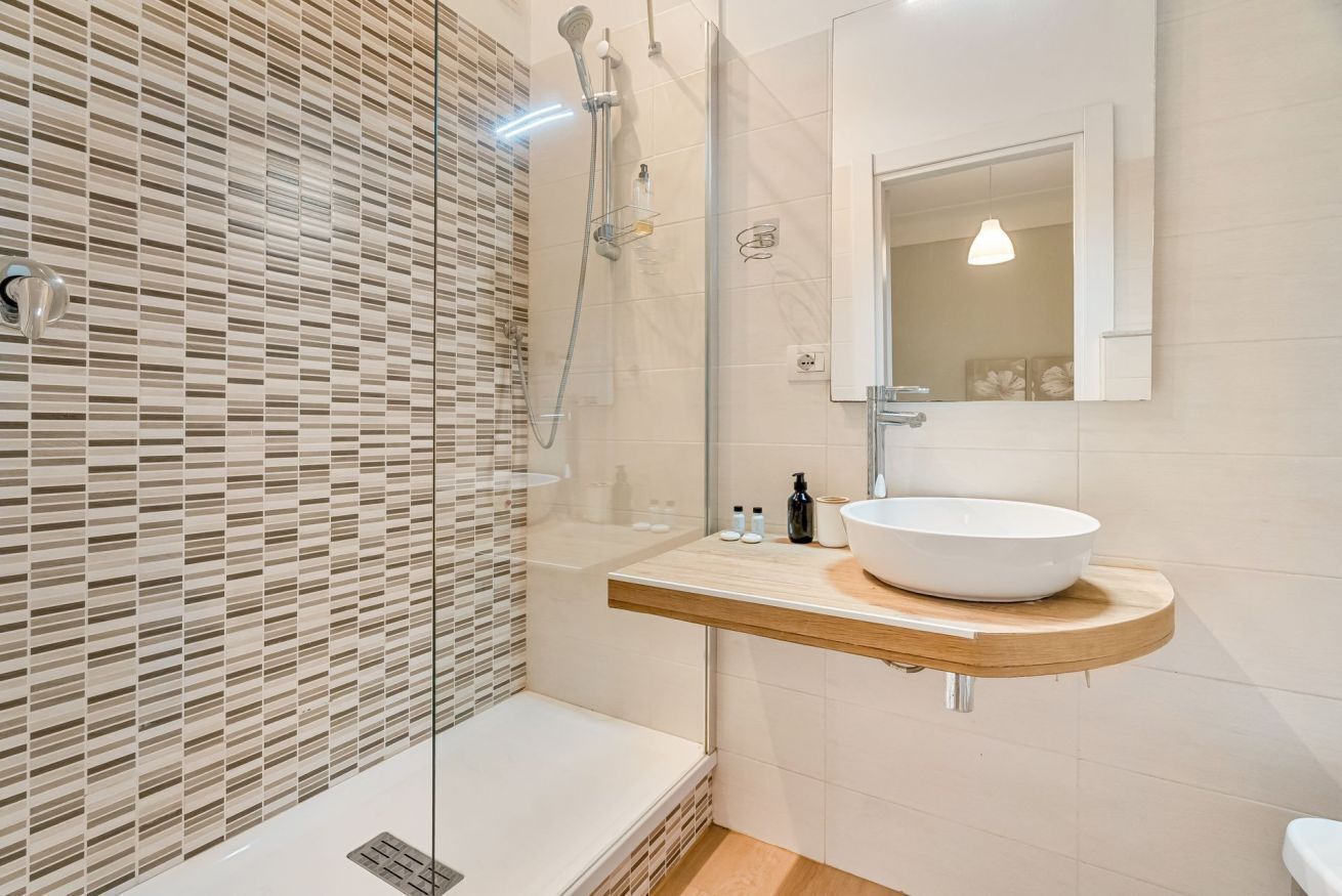 A modern bathroom with a glass-enclosed shower, a wooden vanity with a white sink, and a mirror above the sink.