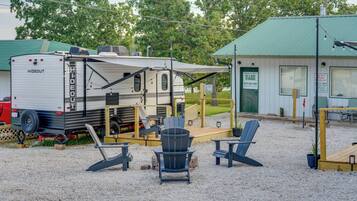 A recreational vehicle (RV) parked in a gravel area with a covered outdoor seating area and a storage building in the background.