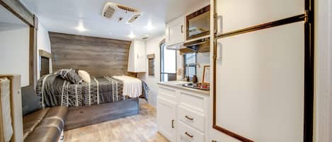 Interior compacto de una caravana con cama, kitchenette y armarios de almacenamiento.