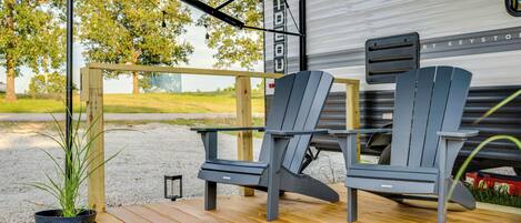 A deck with two Adirondack chairs, a potted plant, and a grill area.