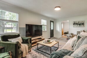 A living room with a large flat-screen TV, green sofas, a coffee table, and a painting on the wall. - Quiet Dayton Monthly Retreat, Near Hospitals (Dayton)