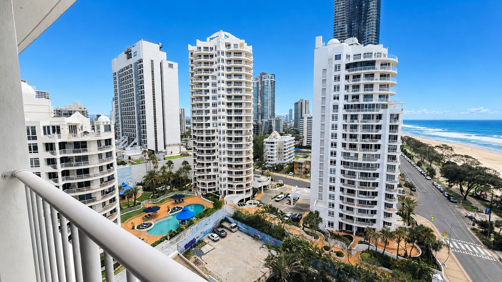 A high-rise residential building with multiple balconies, a swimming pool, and a view of the beach.