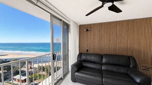 Un balcón con vista a la playa, un sofá de cuero negro y un ventilador de techo.