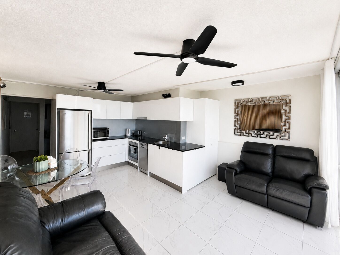 Una sala de estar moderna con un sofá de cuero negro, una mesa de centro de vidrio y un sofá cama de cuero negro.