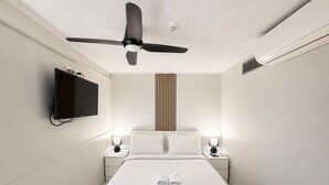 Habitación de hotel con cama, ventilador de techo, televisor montado en la pared y lámparas de noche.