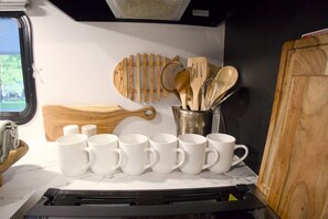 Un coin cuisine comprenant un fourneau, un ensemble de tasses blanches, des ustensiles en bois et une planche à découper.
