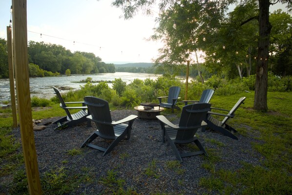 Un espace de détente aménagé au bord de la rivière, avec quatre fauteuils Adirondack et un foyer.