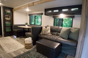 Un intérieur de camping-car compact comprenant un canapé, un pouf et une petite table agrémentée d’une plante.