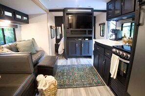 A compact RV interior with a sofa, a kitchen area including a stove and microwave, and a television.