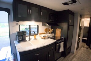 A compact kitchen with dark cabinets, a coffee maker, a sink, and a stove.