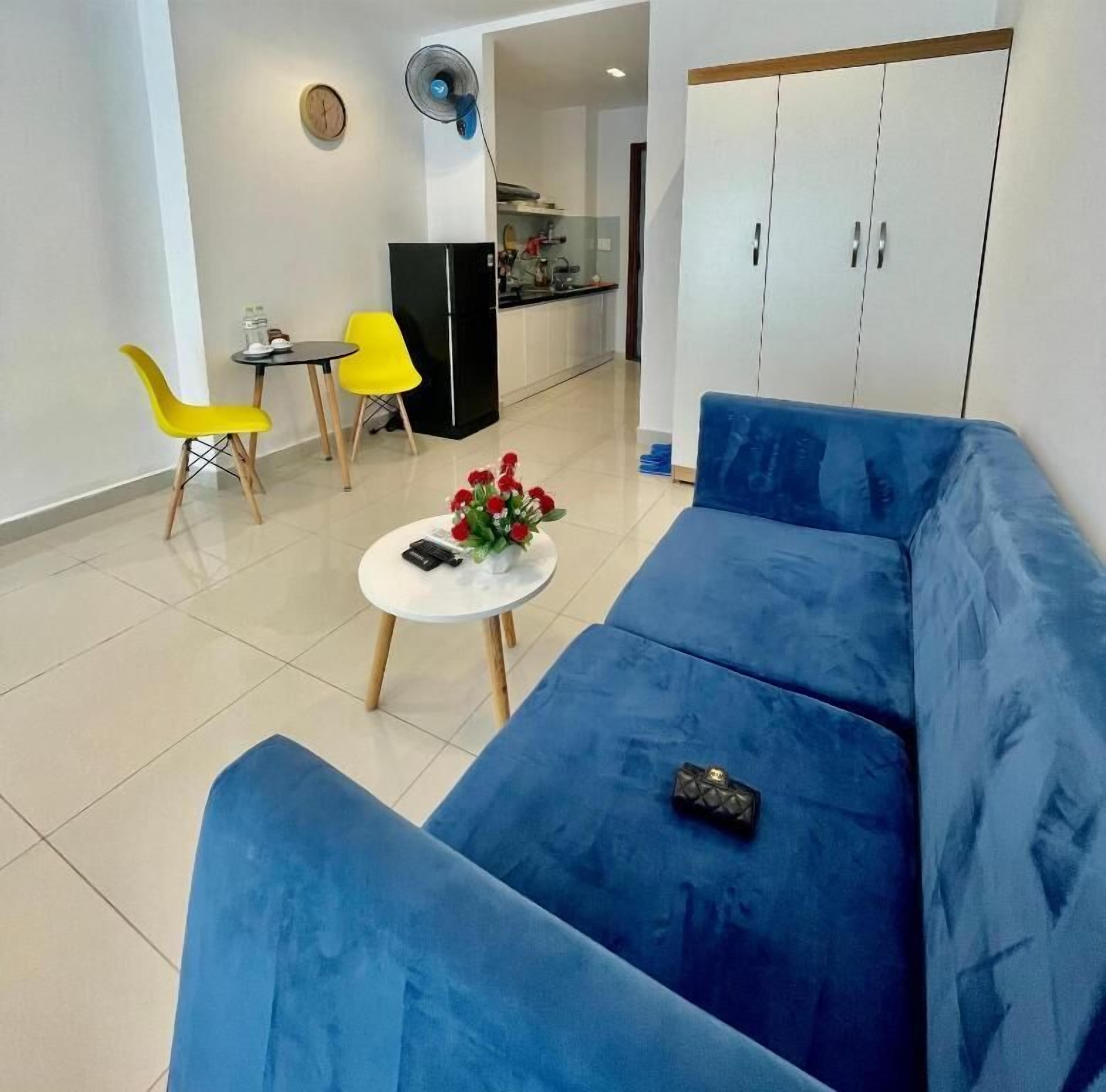 A modern living room with a blue sofa, a small round table with a vase, and two yellow chairs.