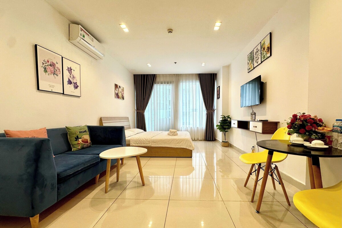 A modern hotel room with a bed, a sofa, a dining table, and a TV.