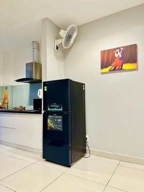 A modern kitchen with a black refrigerator, a wall-mounted fan, and a painting. - Teddy Apartment (Ho Chi Minh City)