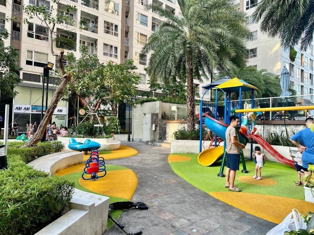 A playground with slides and swings, surrounded by greenery and buildings.