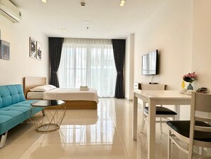 A hotel room with a bed, a blue sofa, a dining table, a TV, and a window with curtains. - Teddy Apartment (Ho Chi Minh City)