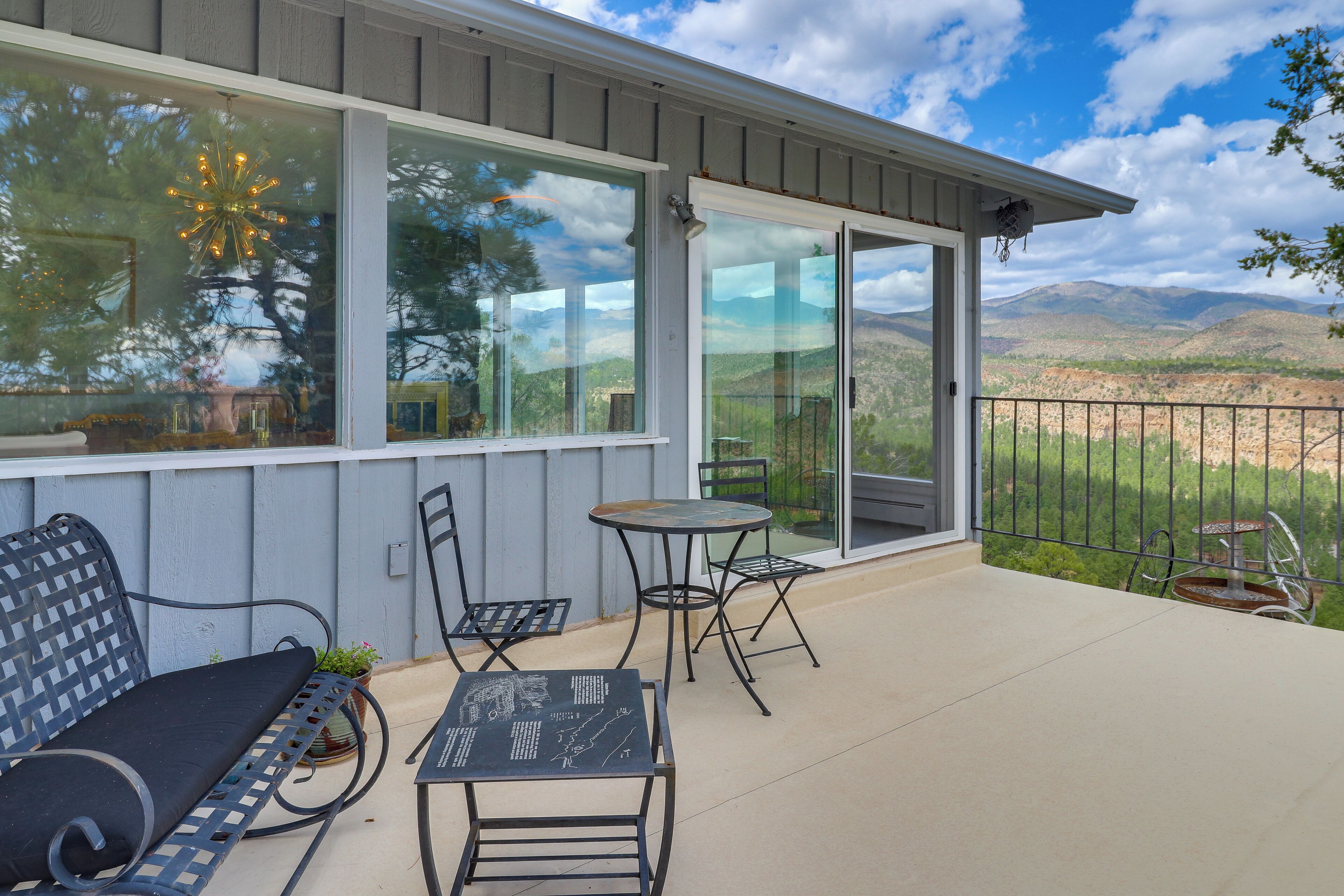 Un patio techado con una mesa, sillas y una banca, y vista a un paisaje montañoso.