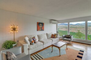 Ein modernes Wohnzimmer mit einem weißen Sofa, einem Couchtisch und Blick auf eine gebirgige Landschaft durch große Fenster.