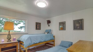 Ein Schlafzimmer mit zwei Einzelbetten, einem Nachttisch, einer Lampe und einem Fenster mit Blick auf Bäume.