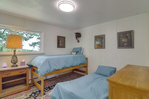 Ein Schlafzimmer mit zwei Einzelbetten, einem Nachttisch, einer Lampe und einem Fenster mit Blick auf Bäume.