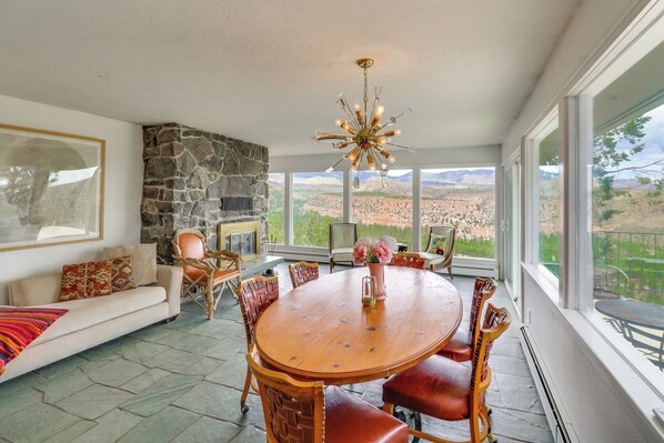A spacious living area with a stone fireplace, a dining table with chairs, and large windows offering a view of the mountains.