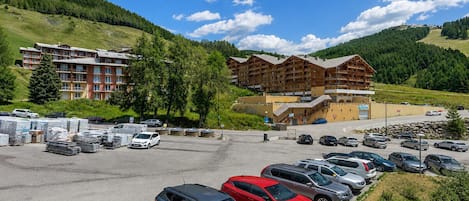 A hotel with multiple floors, a parking lot with various vehicles, and a mountainous backdrop.