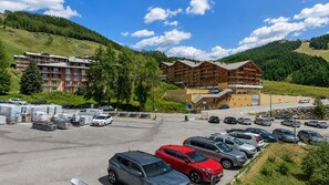 A hotel with multiple floors, a parking lot with various vehicles, and a mountainous backdrop. - Studio with views of the ski slopes and a mountain-themed area (Allos)