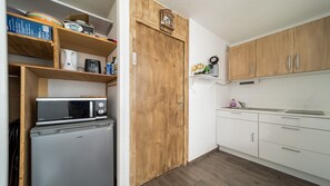 A compact kitchen with wooden cabinets, a microwave, a refrigerator, and a small shelf with various items. - Studio with views of the ski slopes and a mountain-themed area (Allos)