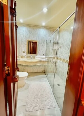 Un baño con cabina de ducha de vidrio, inodoro blanco y suelo de mármol.
