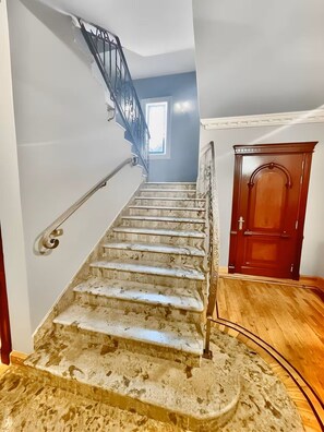 Una escalera con barandilla, una puerta de madera y una ventana al fondo.