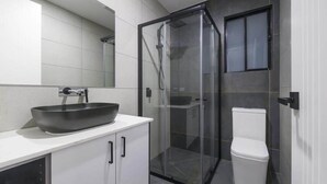 Uma casa de banho moderna com cabine de duche em vidro, lavatório branco com cuba grande e sanita.
